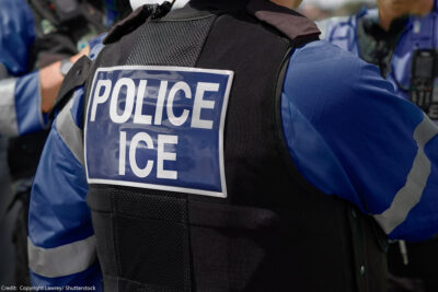 Close-up of POLICE ICE marking on the back of a vest uniform worn by a trio of officers.