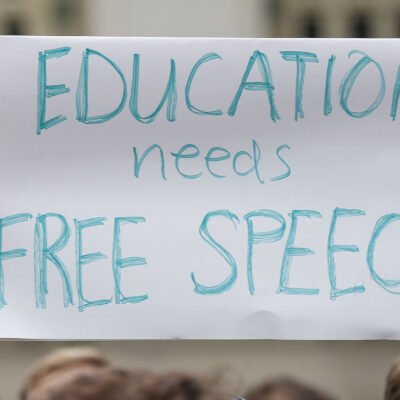 A student holds up a placard reading 'Education needs free speech' while attending a march.