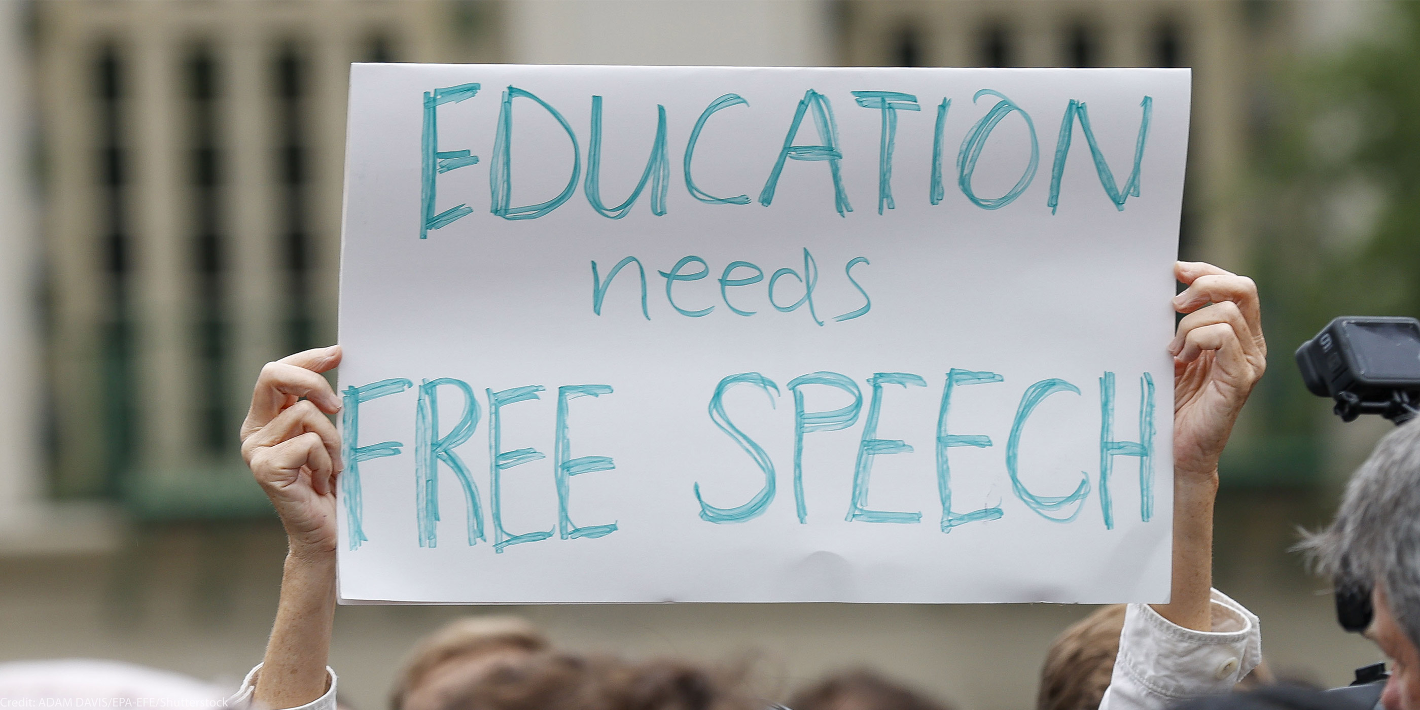 A student holds up a placard reading 'Education needs free speech' while attending a march.