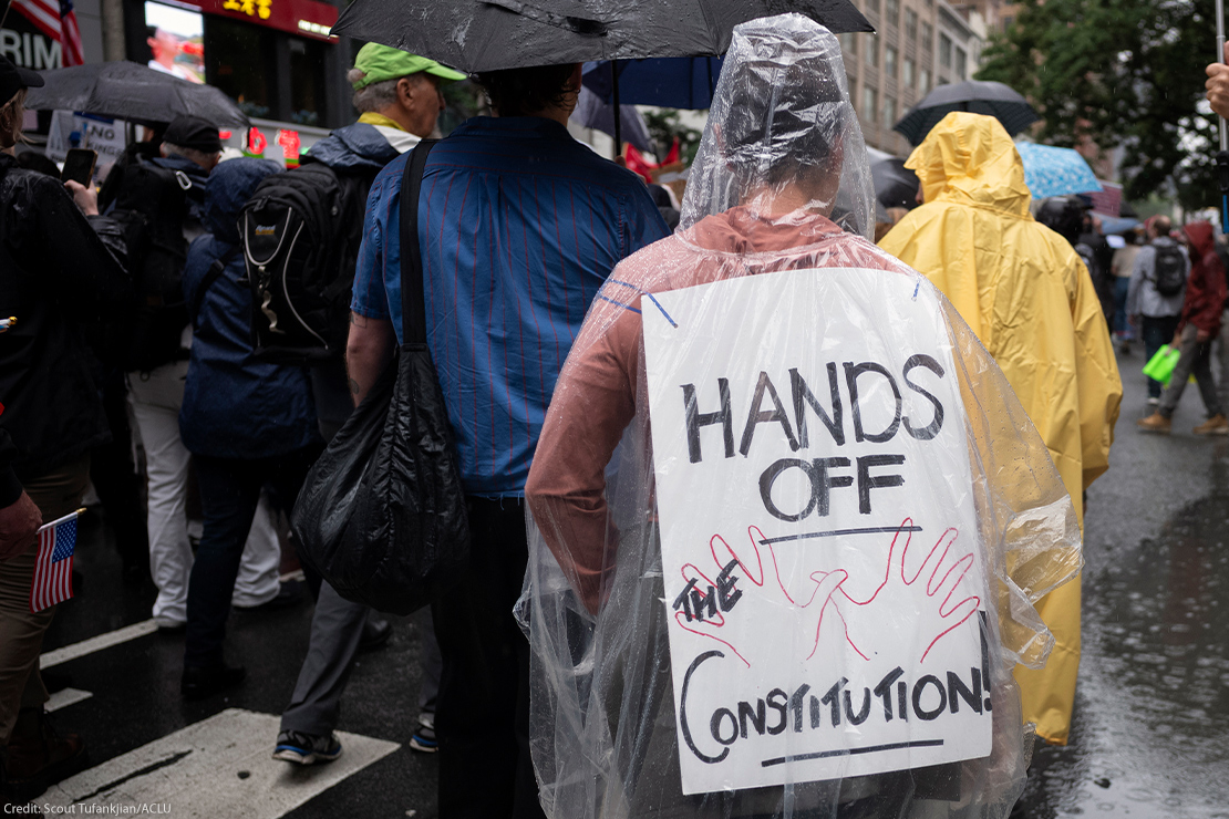A person wearing a clear poncho displays a sign on their back that reads "HANDS OFF THE CONSTITUTION" while walking in the rain as they take part with thousands of other New Yorkers take part in the NO KINGS national day of action.