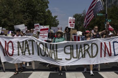 Demonstrators march in Washington, DC carrying a banner that reads " NO NATIONAL GUARD IN DC".