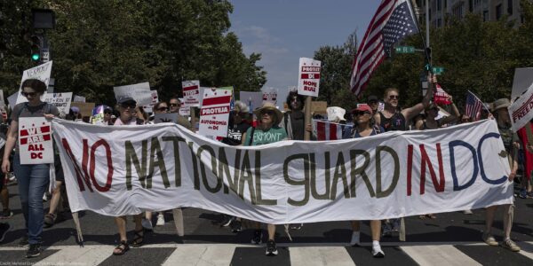 Demonstrators march in Washington, DC carrying a banner that reads " NO NATIONAL GUARD IN DC".