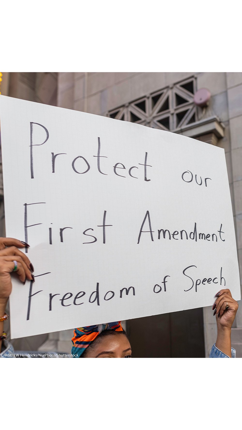 A person holds a large handwritten sign reading “Protect our First Amendment Freedom of Speech” during a protest outside the El Capitan Entertainment Centre, where Jimmy Kimmel Live! is filmed. Behind them, another protester in a skeleton costume holds a cardboard sign depicting a crossed-out image of Jimmy Kimmel. The demonstration is in response to ABC’s decision to pull Kimmel off the air following his remarks about Charlie Kirk.
