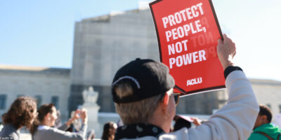An individual holding a sign that says "Protect People, Not Power" outside of the U.S. Supreme Court ahead of arguments in the Voting Rights case Callais v. Landry.