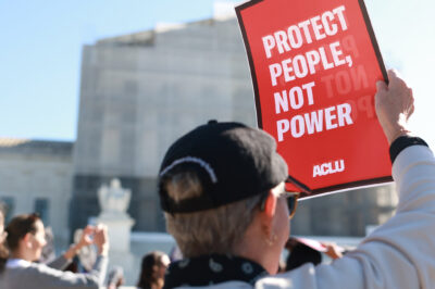 An individual holding a sign that says "Protect People, Not Power" outside of the U.S. Supreme Court ahead of arguments in the Voting Rights case Callais v. Landry.